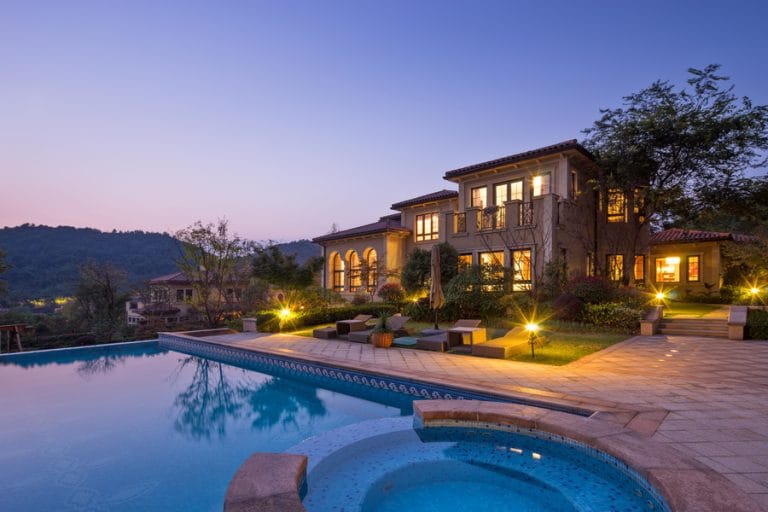 Luxury home at dusk with pool, spa, and elegant outdoor lighting illuminating the landscape.