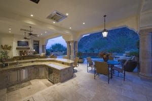 A modern marble kitchen with a wall open to an elegant patio with a hill beyond it.
