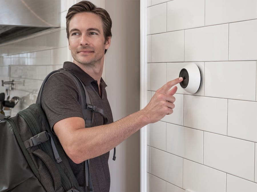 Man standing by the door beside a Josh.ai wall-mounted device.